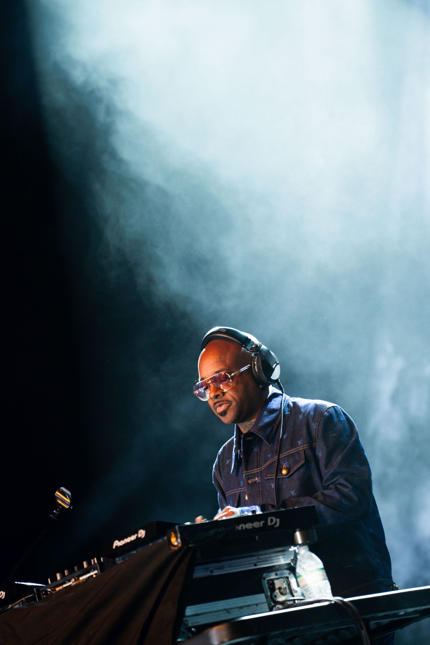 DJ performing at a concert with electronic equipment surrounded by atmospheric smoke effects.