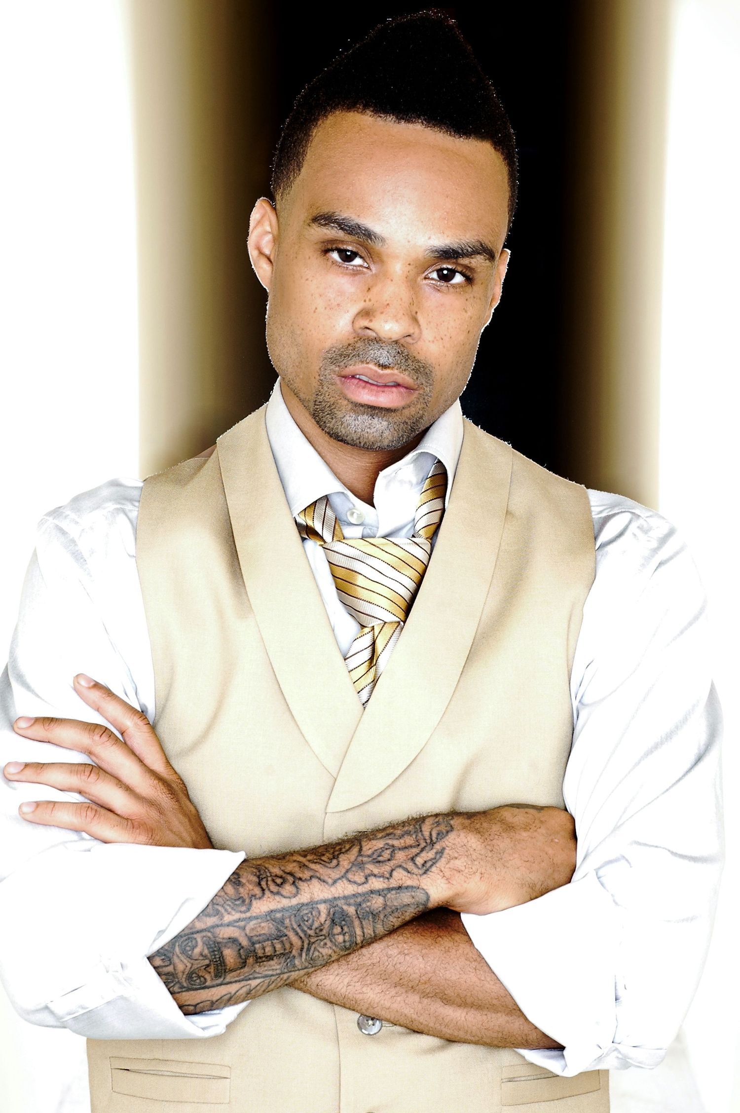 Artistic portrait of a man in formal vest and tie with visible arm tattoo.