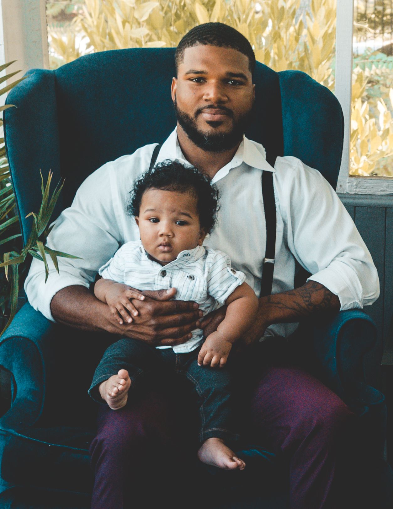 A parent and child sit together in a teal velvet chair in a series of intimate portrait photographs.