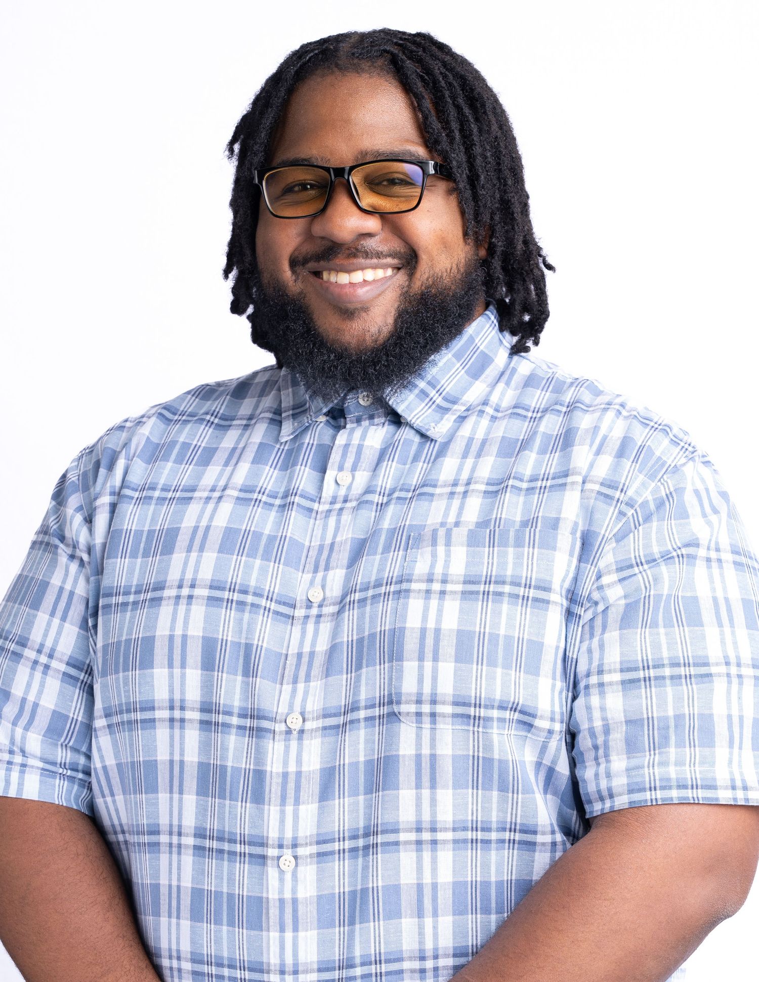 Professional headshot of person wearing glasses and a blue plaid short-sleeve button-up shirt smiles warmly at the camera.