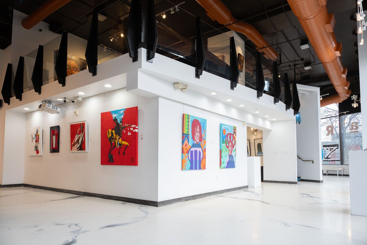 Modern art gallery interior with white walls, exposed wooden beams, and colorful framed artwork displayed along the walls.