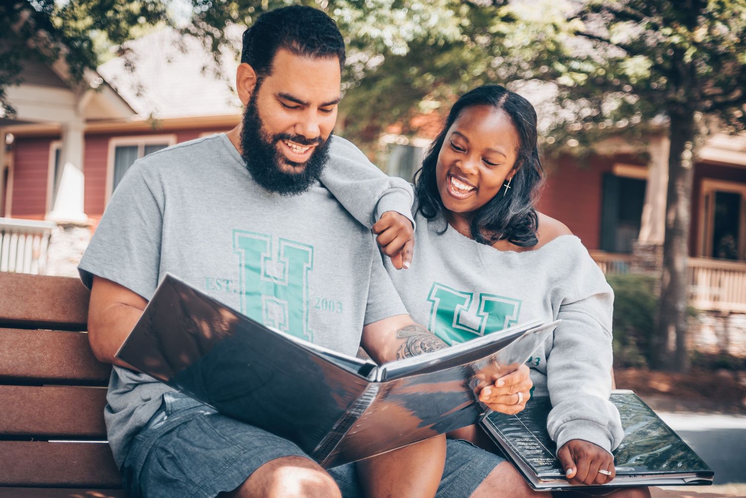 Two people share a joyful moment while looking at a book together on a park bench.