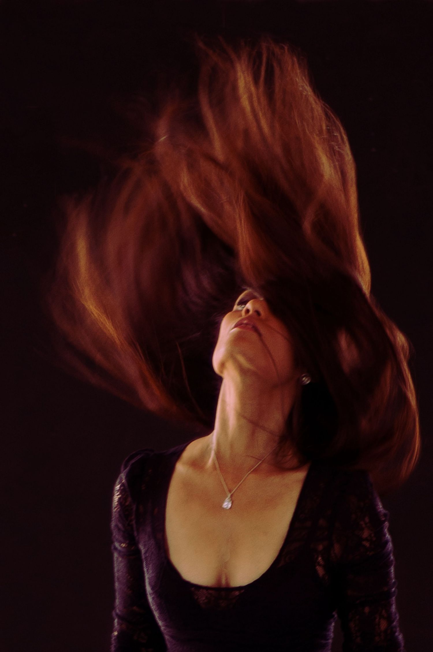 Woman with flowing red hair in a black top shown in a dynamic hair-flipping motion sequence against dark background.