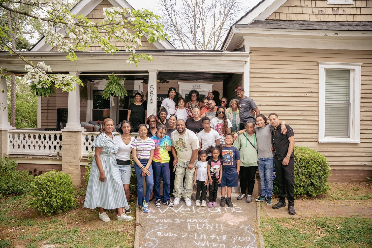 Large diverse family group posing together in front of a charming historic home during a spring gathering.