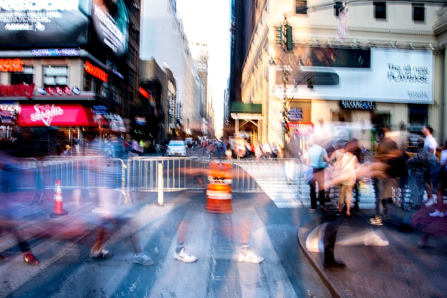 Blurred urban street scene with motion-captured pedestrians and vehicles in a city setting.