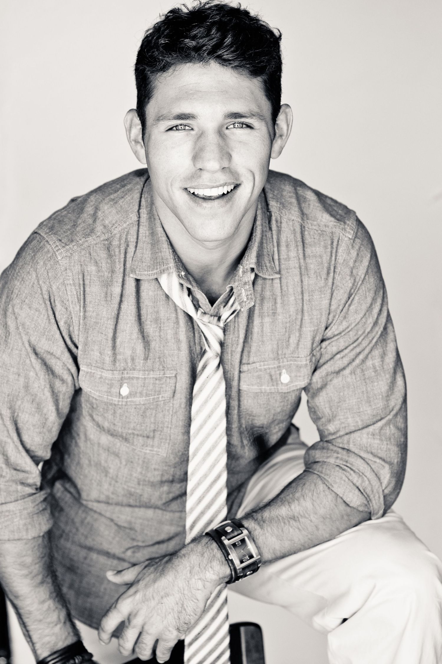 Black and white portrait  showing a person in a gray button-down shirt and striped tie against white background.
