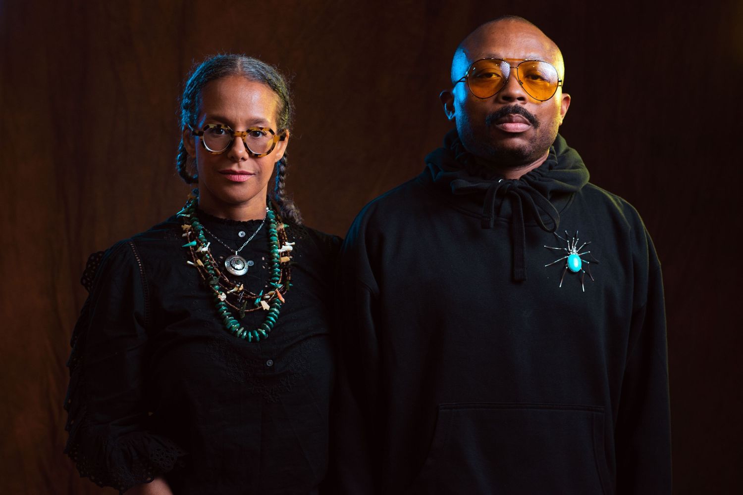 Couple portrait in dark setting with people wearing black clothing and statement necklaces.