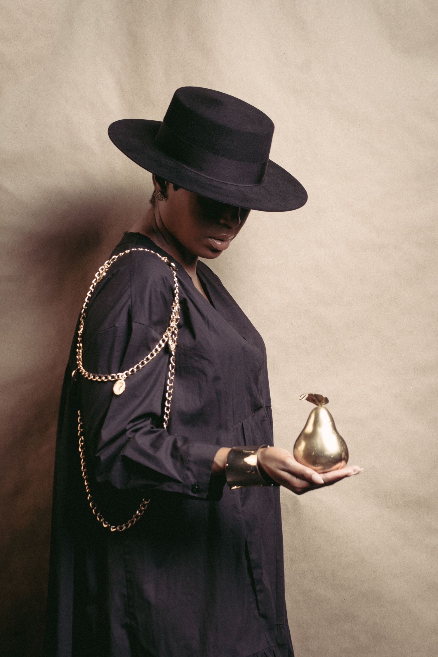 Stylized fashion portraits featuring figure in black outfit and hat with gold chain accessories.