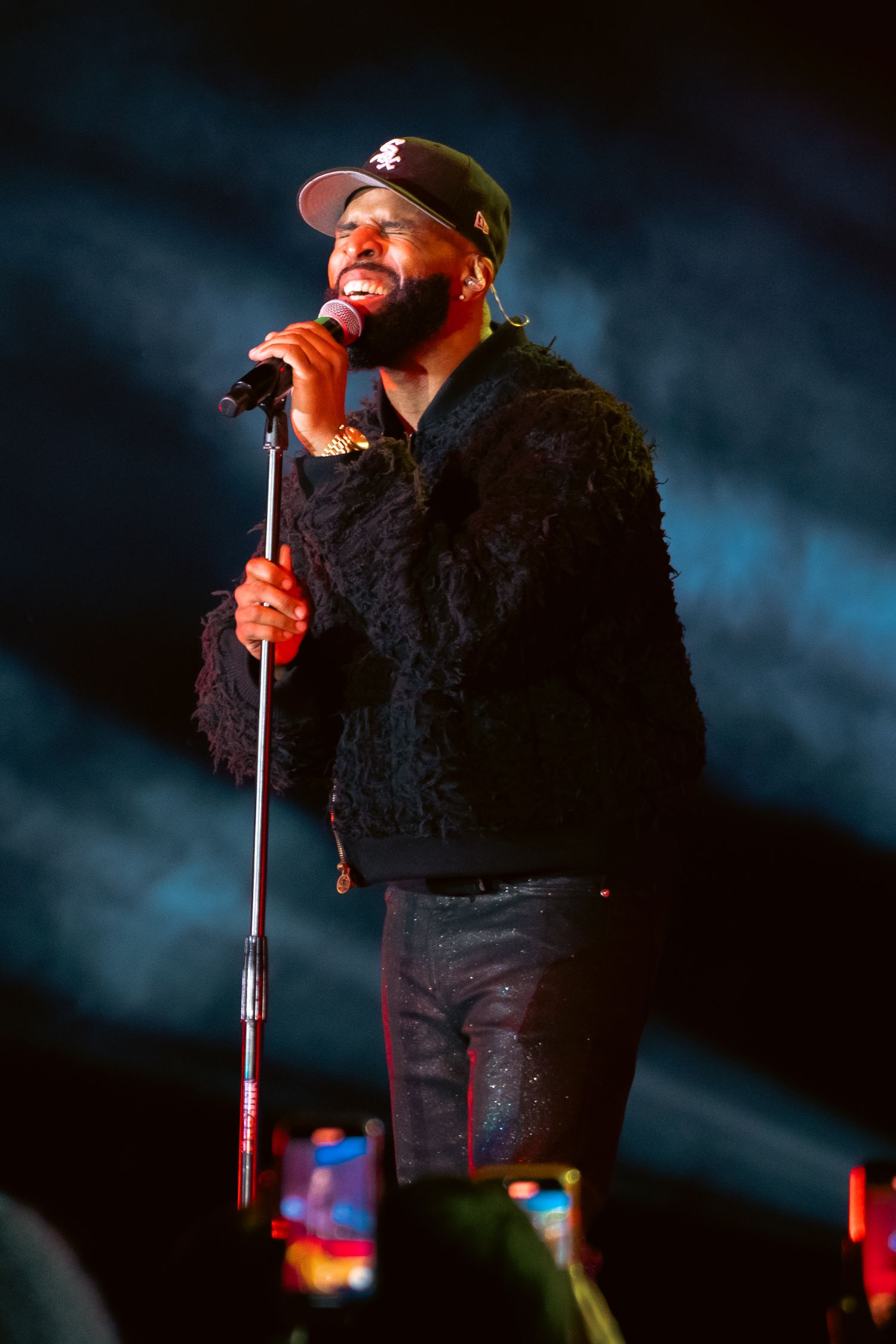 Performer in black clothing singing passionately on stage with dramatic lighting.