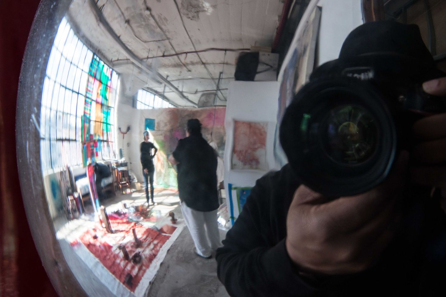 A fisheye lens view of a photographer with camera equipment in an industrial space with large windows and exposed ceiling.
