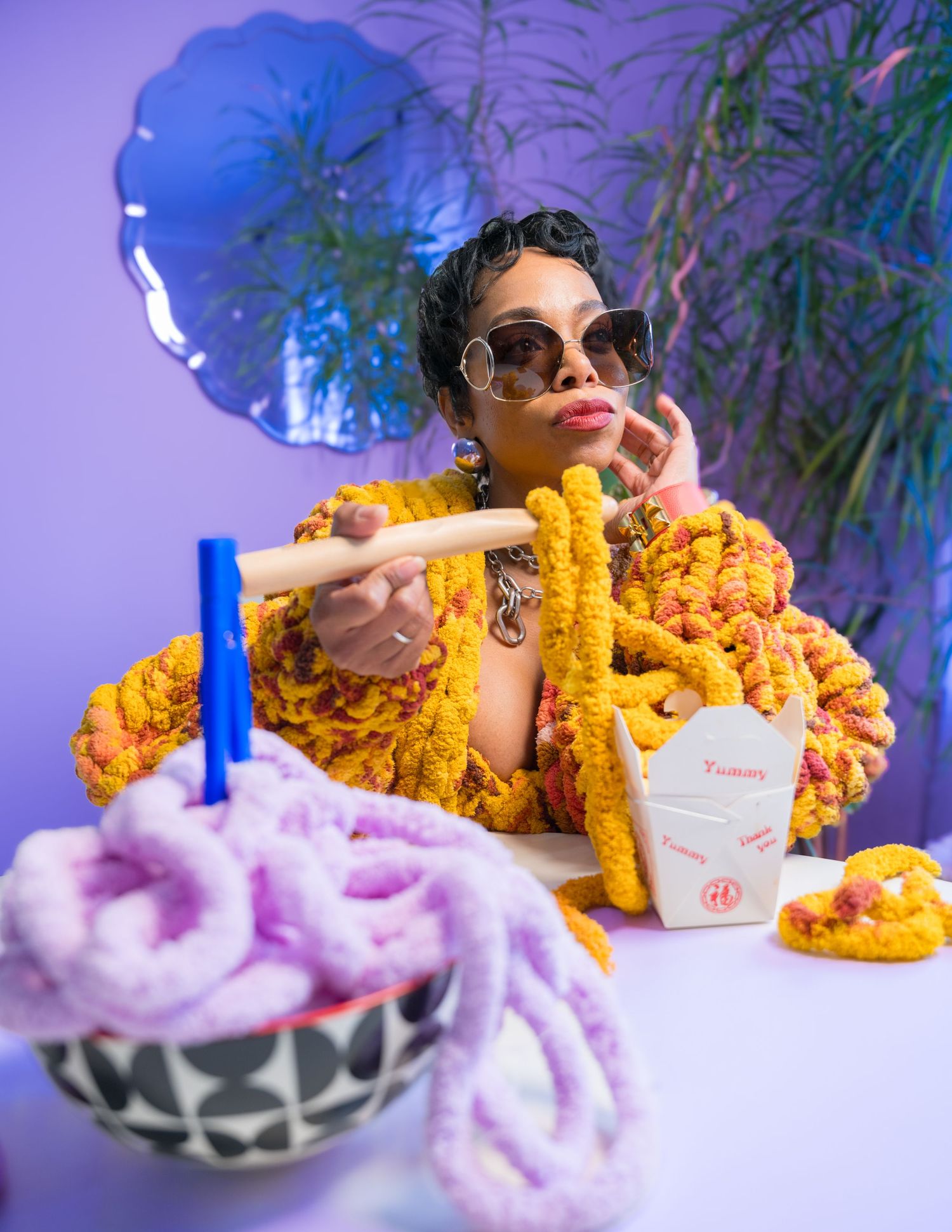 A person in sunglasses poses with bright orange curly fries and cotton candy against a blue background.