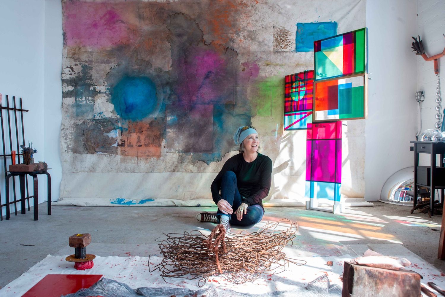 An artist sits on the floor of a colorful studio space with stained glass effects.