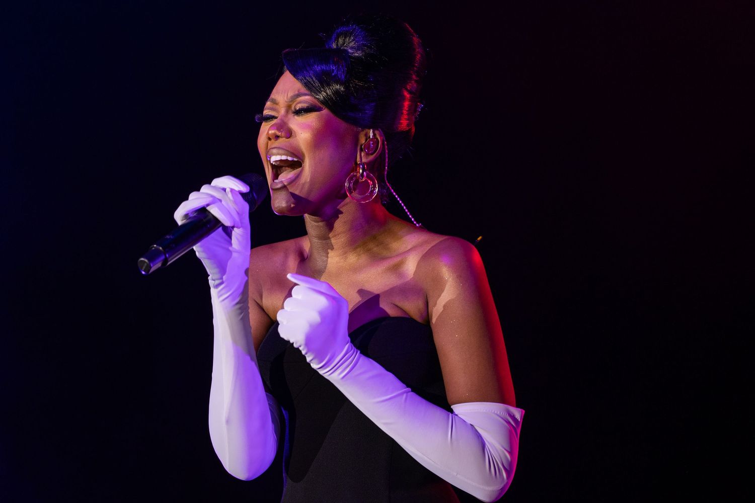 Concert performer singing emotionally into microphone with dramatic stage lighting.
