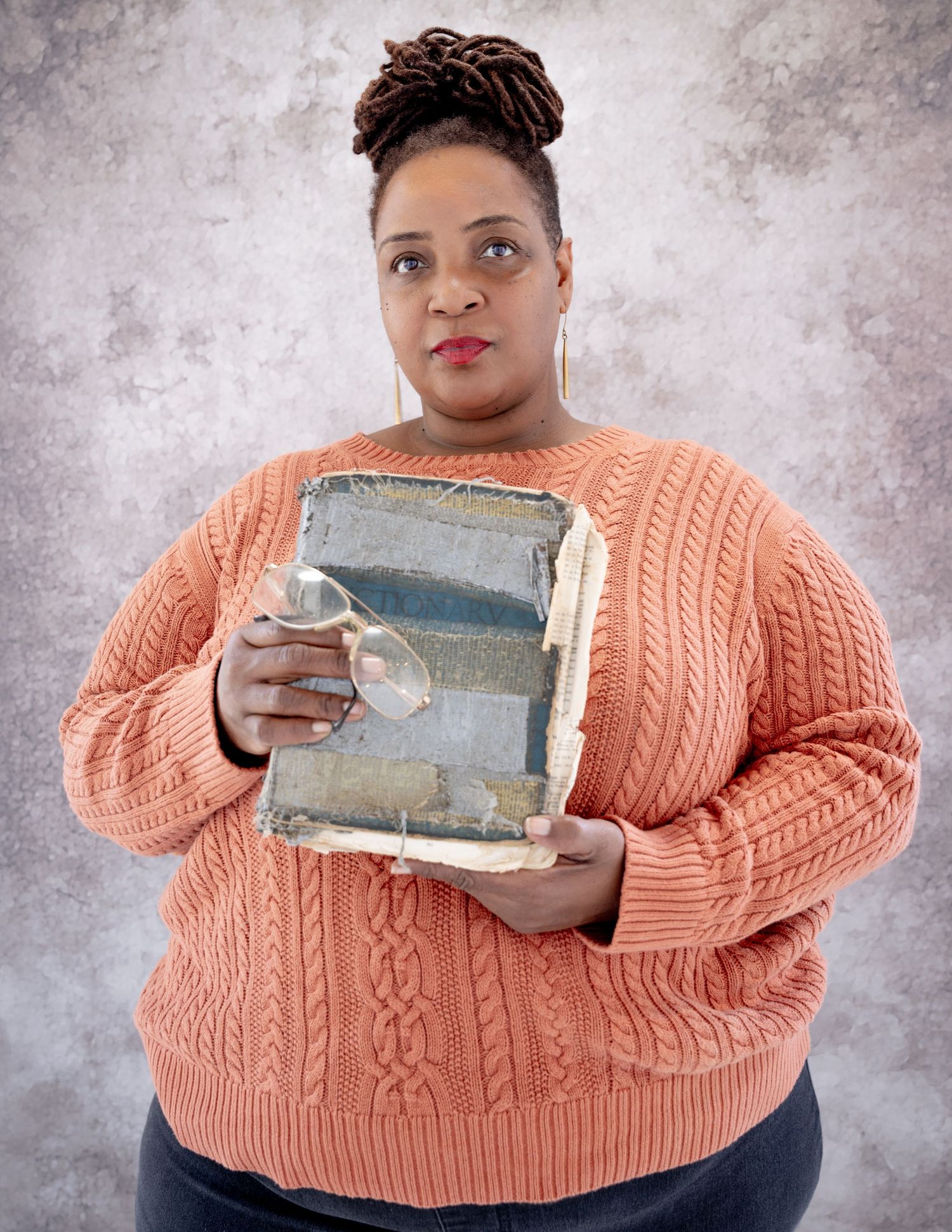 Person in a coral sweater holding a vintage book with glasses for Labor Of Love series.