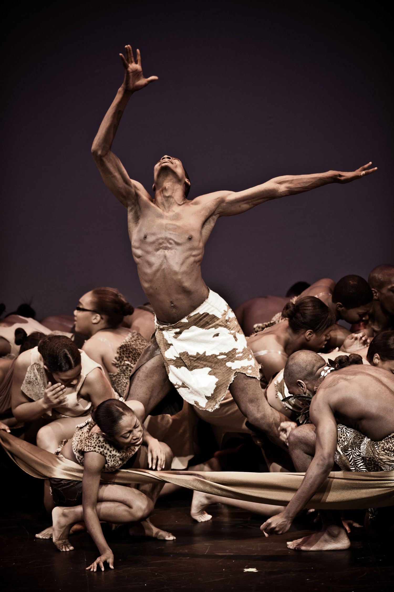 Modern dancers perform an emotional contemporary dance piece in sepia tones on a dark stage.