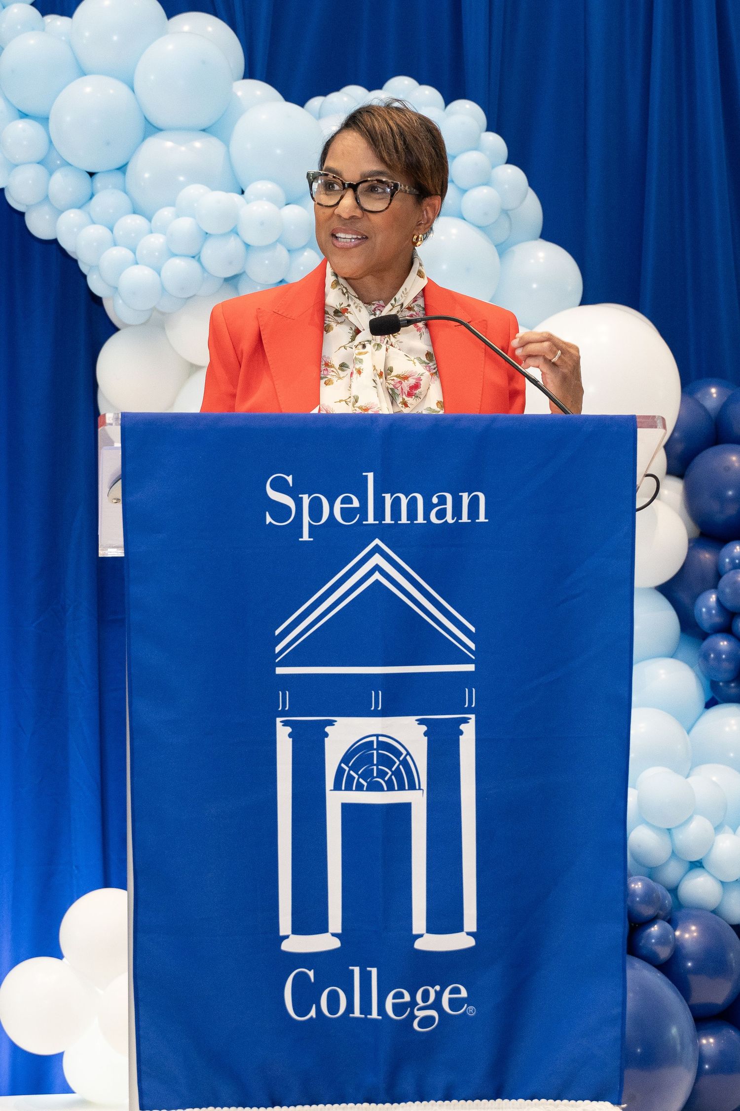 Speaker at a Spelman College podium with blue and white balloon decorations in the background.