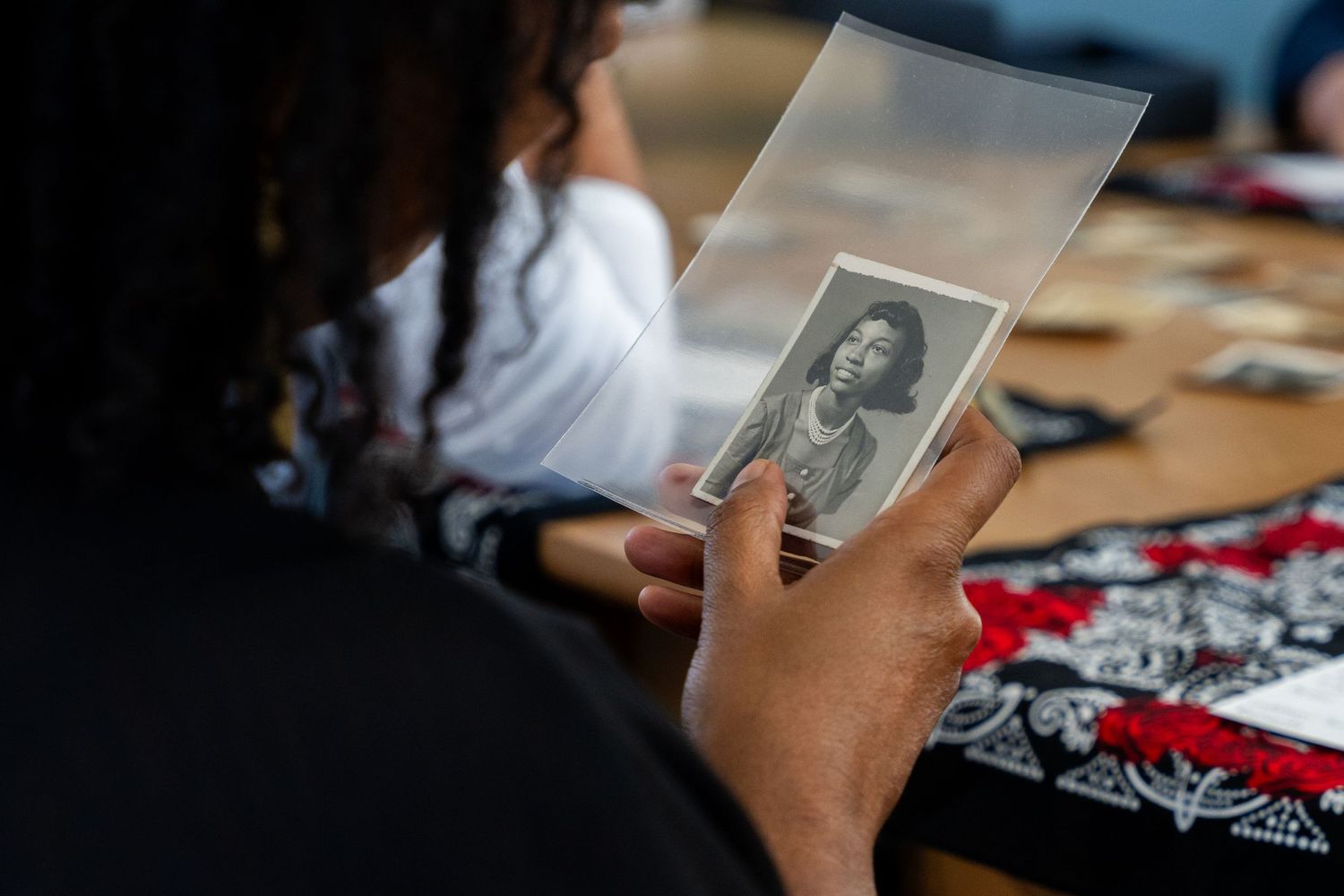 Someone holds an old black and white photograph in a clear protective sleeve while sitting at a table.