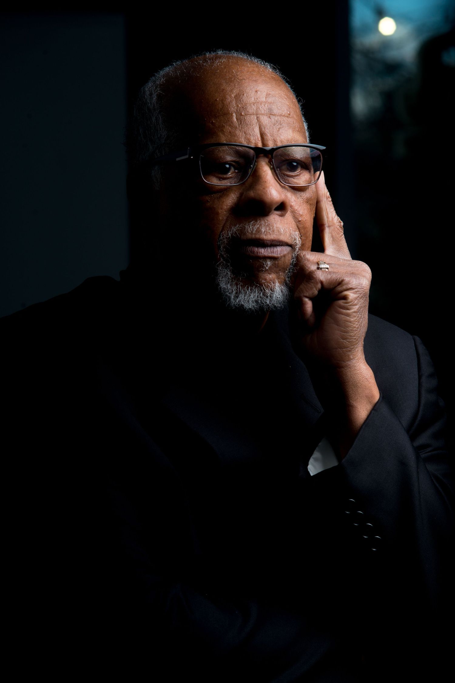 A dramatic portrait series in dark lighting shows a person wearing glasses and a suit against a black background.