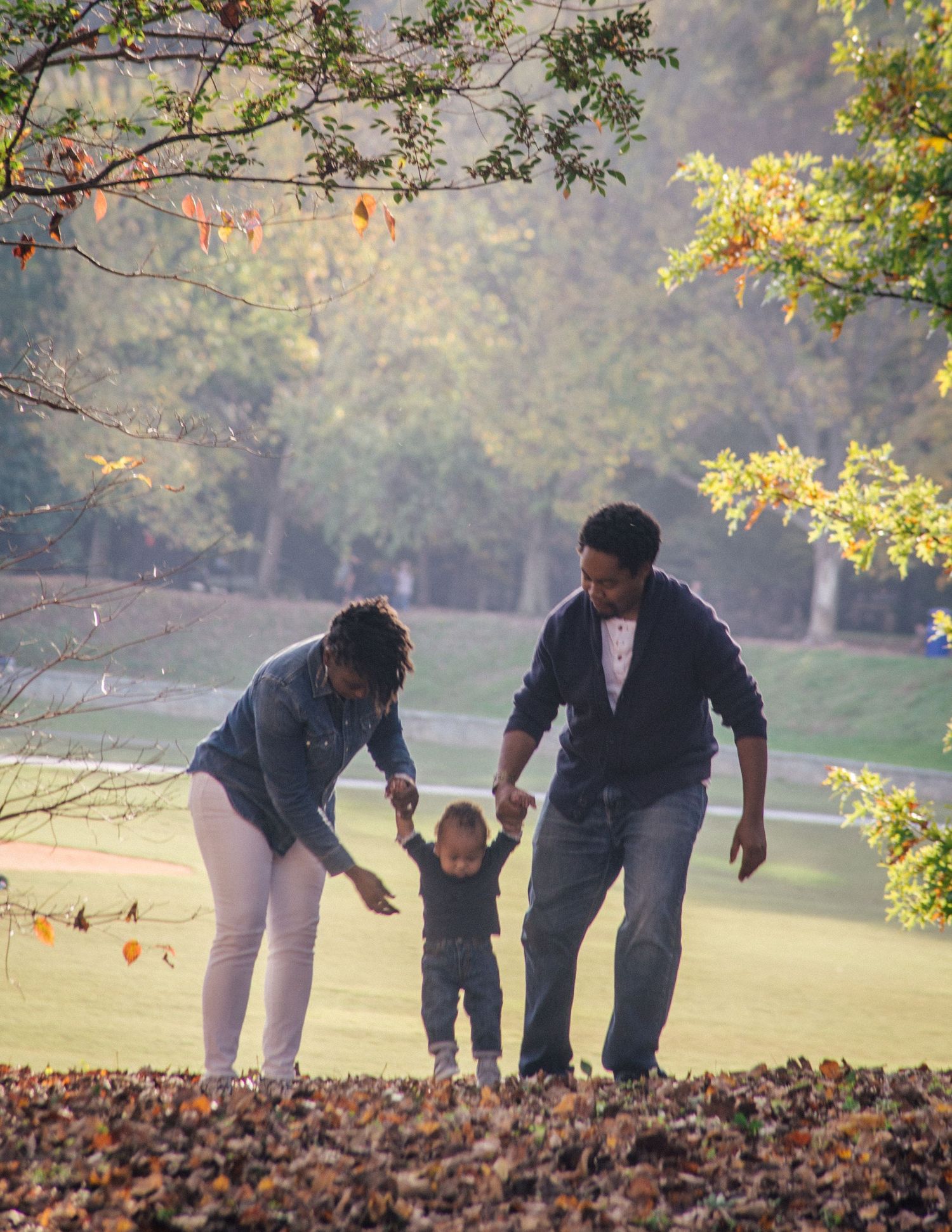 A family with a toddler enjoying an autumn day in a park, with colorful fall foliage in the background.