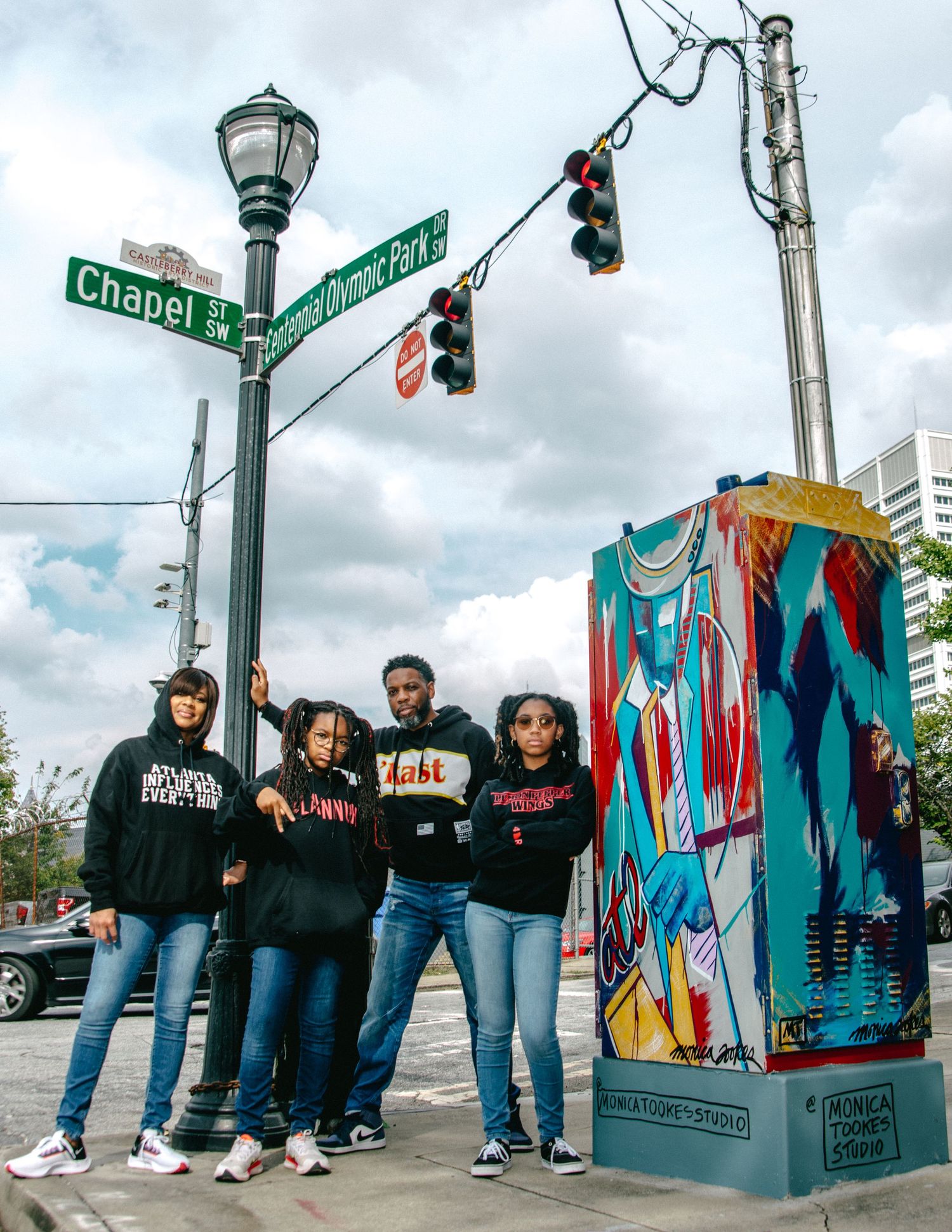 Group of people posing together on a city street corner with colorful street art and traffic signals in the background.