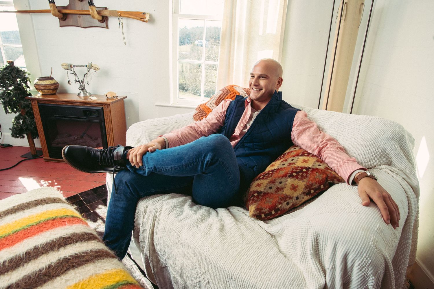 A person relaxes on a cozy couch with colorful striped pillows in a sunlit living room.