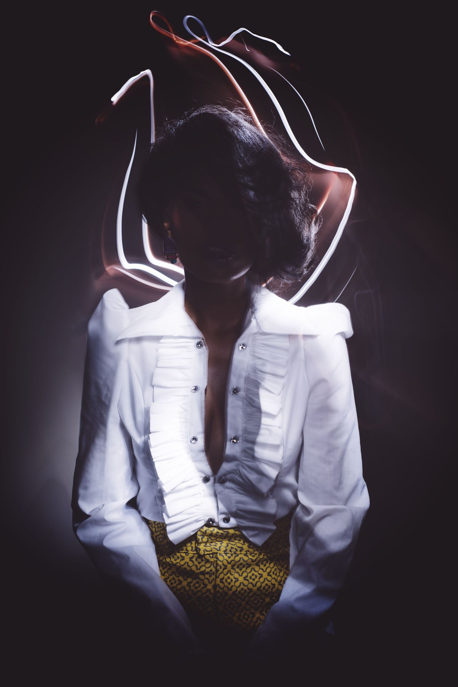 Artistic portrait with light trails around a silhouette wearing a white button-up shirt and patterned belt against dark background.