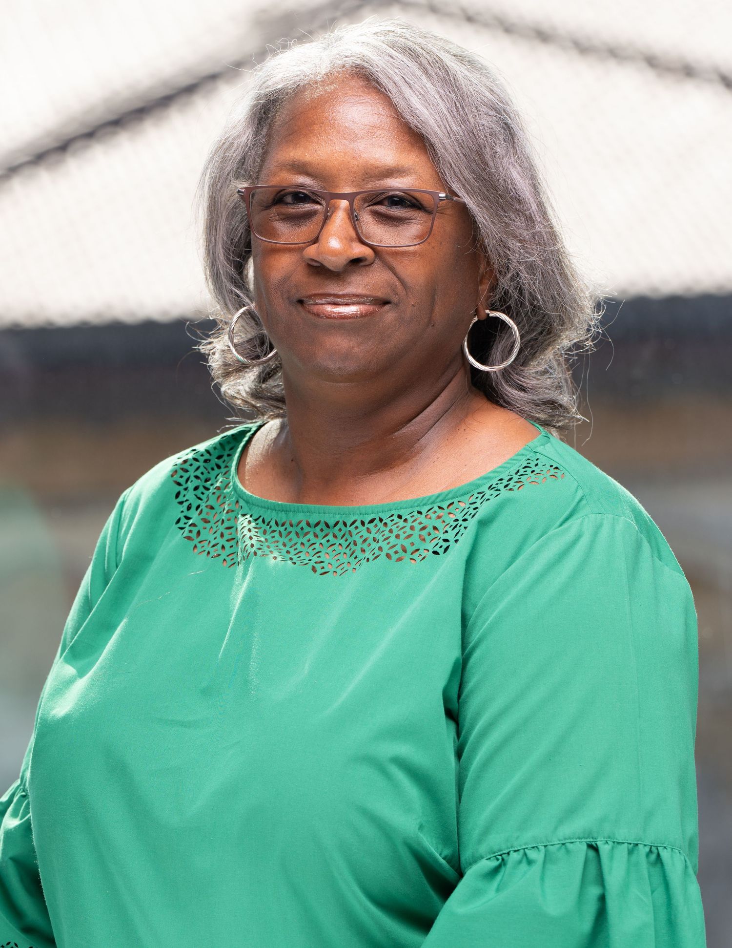 Professional headshot of person wearing a bright green embellished top and glasses smiles warmly while posing for a photo.