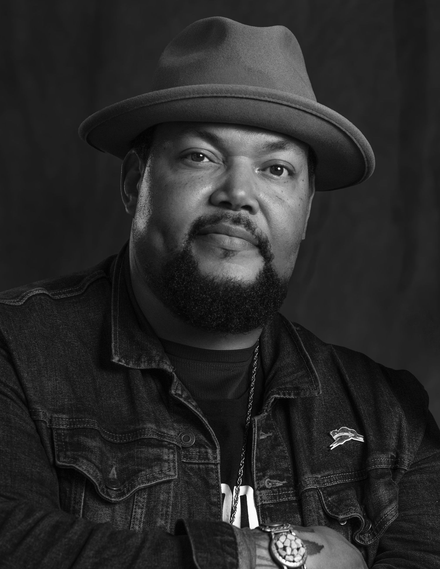 A black and white portrait series showing a dramatic angle of a John Stephens wearing a hat and denim jacket.