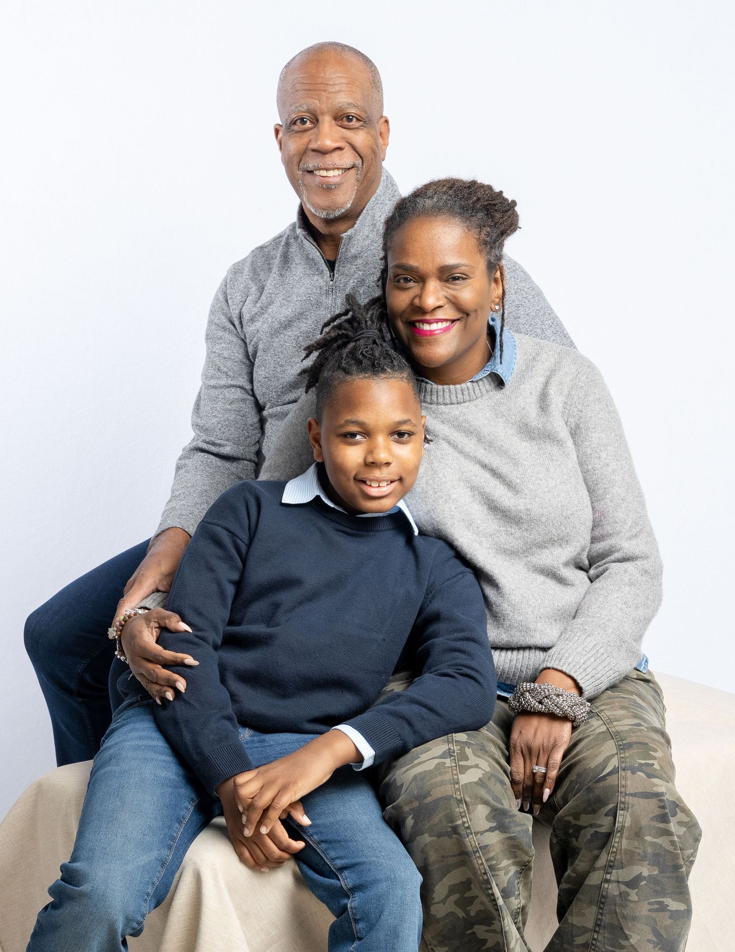 A family of three sits together on a white background in a series of casual portrait poses.