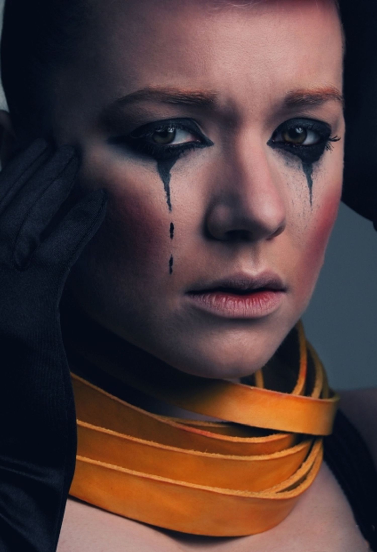 Artistic portrait with dramatic makeup and orange collar showing black tears.