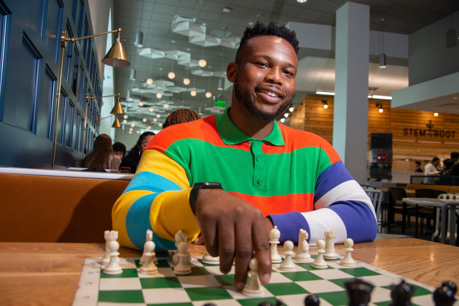 Student concentrates while playing chess at a wooden table in a bright indoor space.