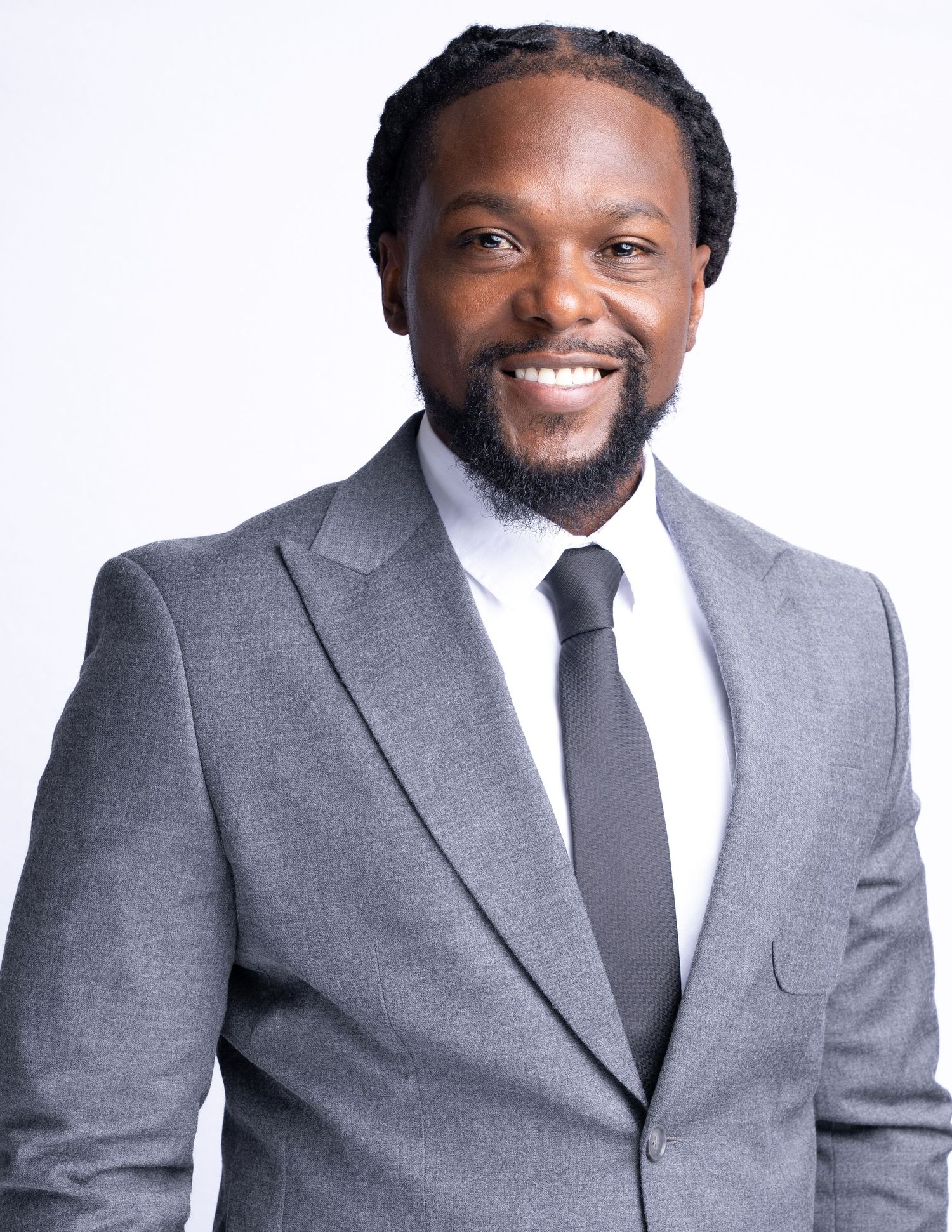 Professional headshot of someone wearing a gray suit and dark tie with a warm smile against a white background.