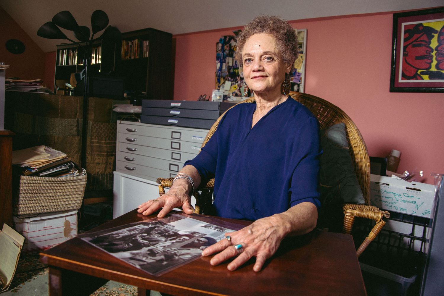 Person in blue shirt examining photographs at a desk in a home office setting.