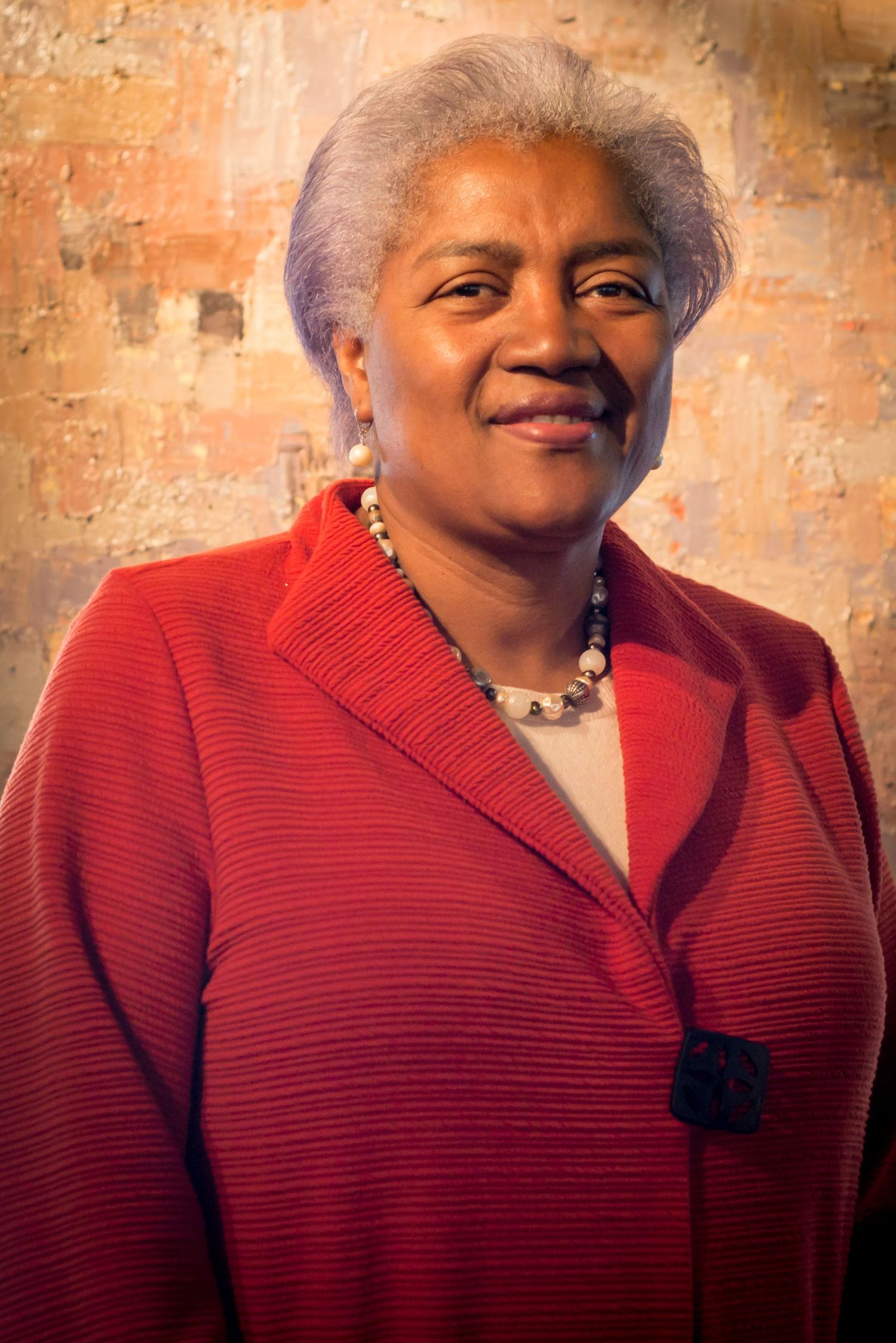 Portrait of someone wearing a bright red textured sweater against a warm brick wall.