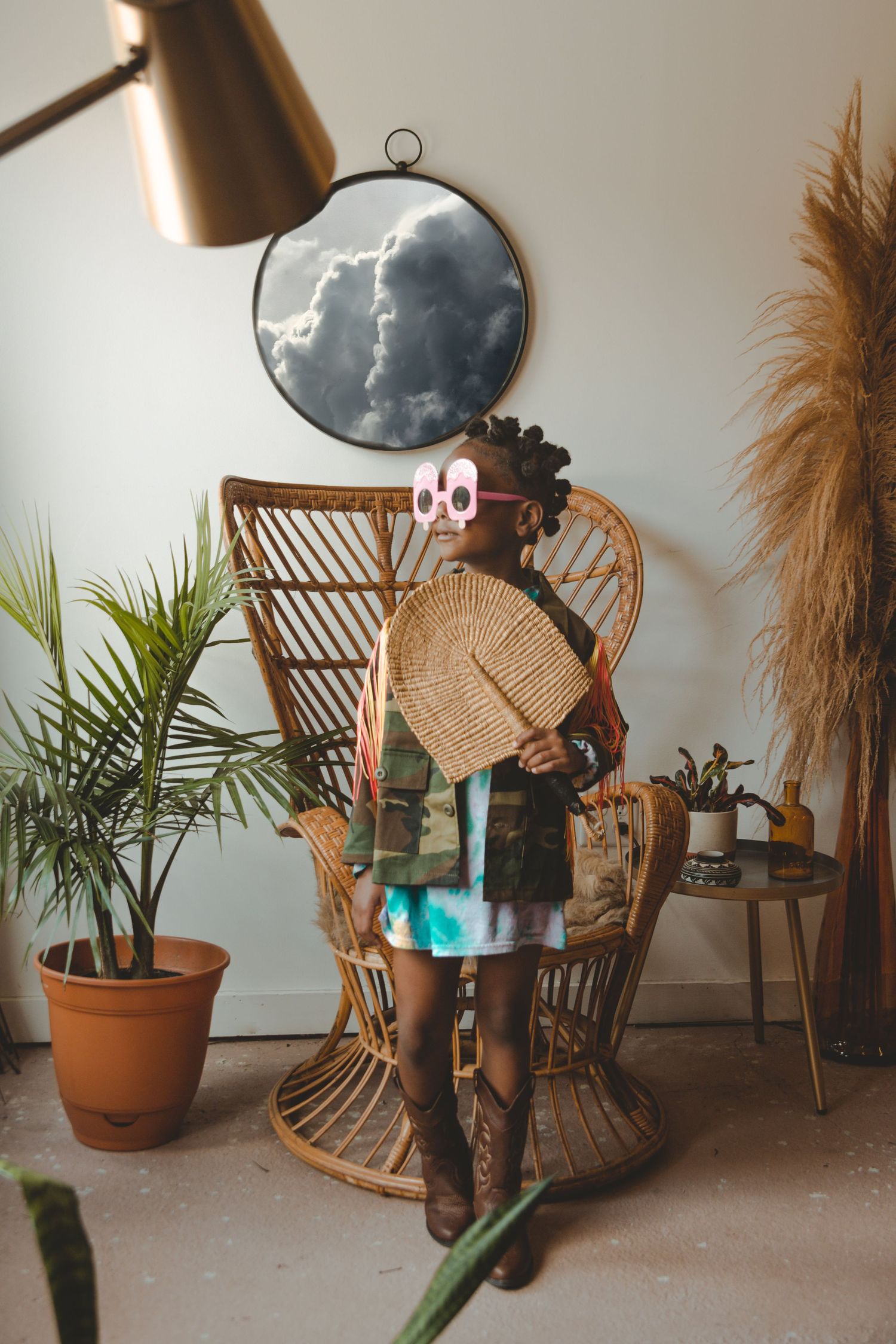 Portrait of young person with wicker peacock chair styled in background with plants and decorative elements in bright interior space.