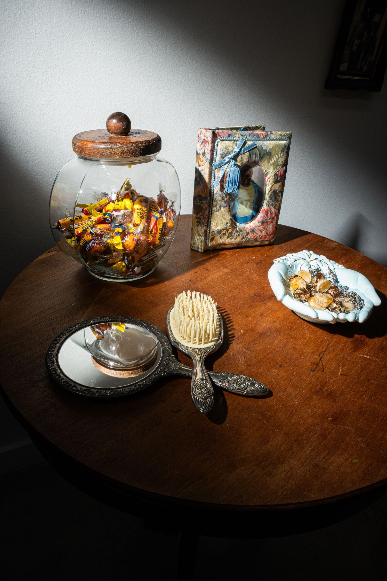 A vintage table setting with a glass jar of dried flowers, antique brush, decorative box, and plates in dramatic lighting.