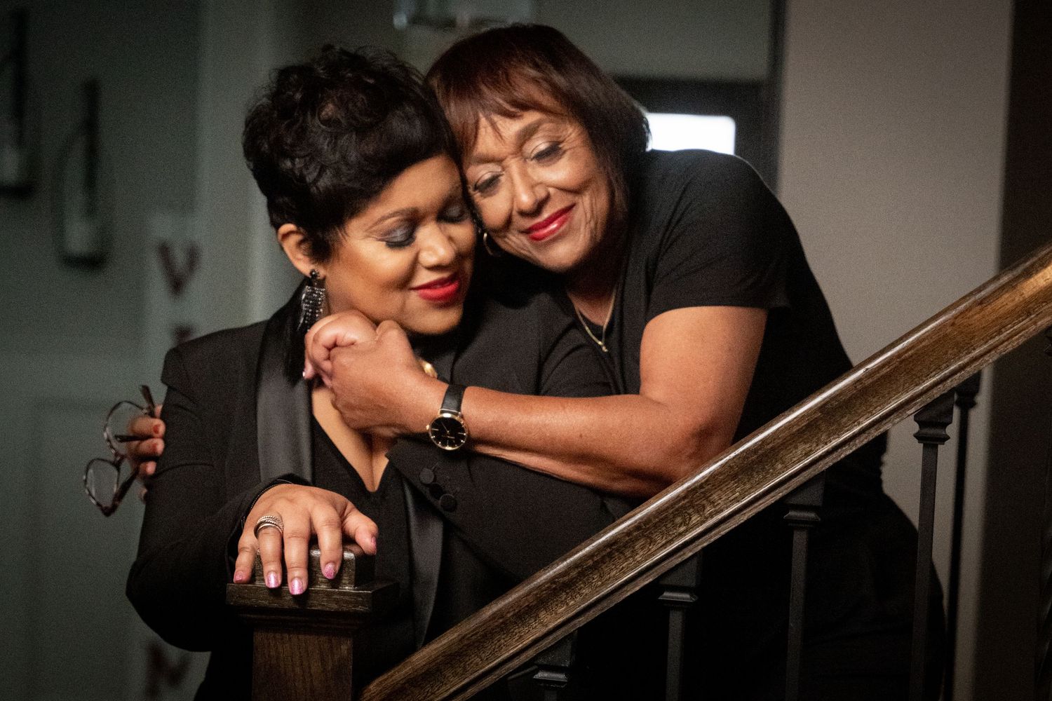 Mother and daughter sharing an intimate moment near a wooden banister in low light.
