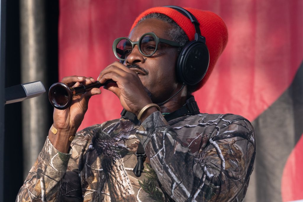 Performer wearing camouflage and red cap with headphones against a vibrant red backdrop.