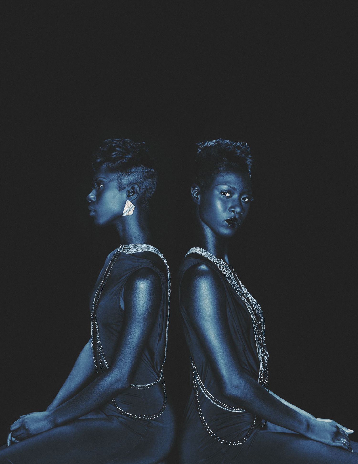 Artistic portrait of two women in dark lighting with blue tones and chain accessories.