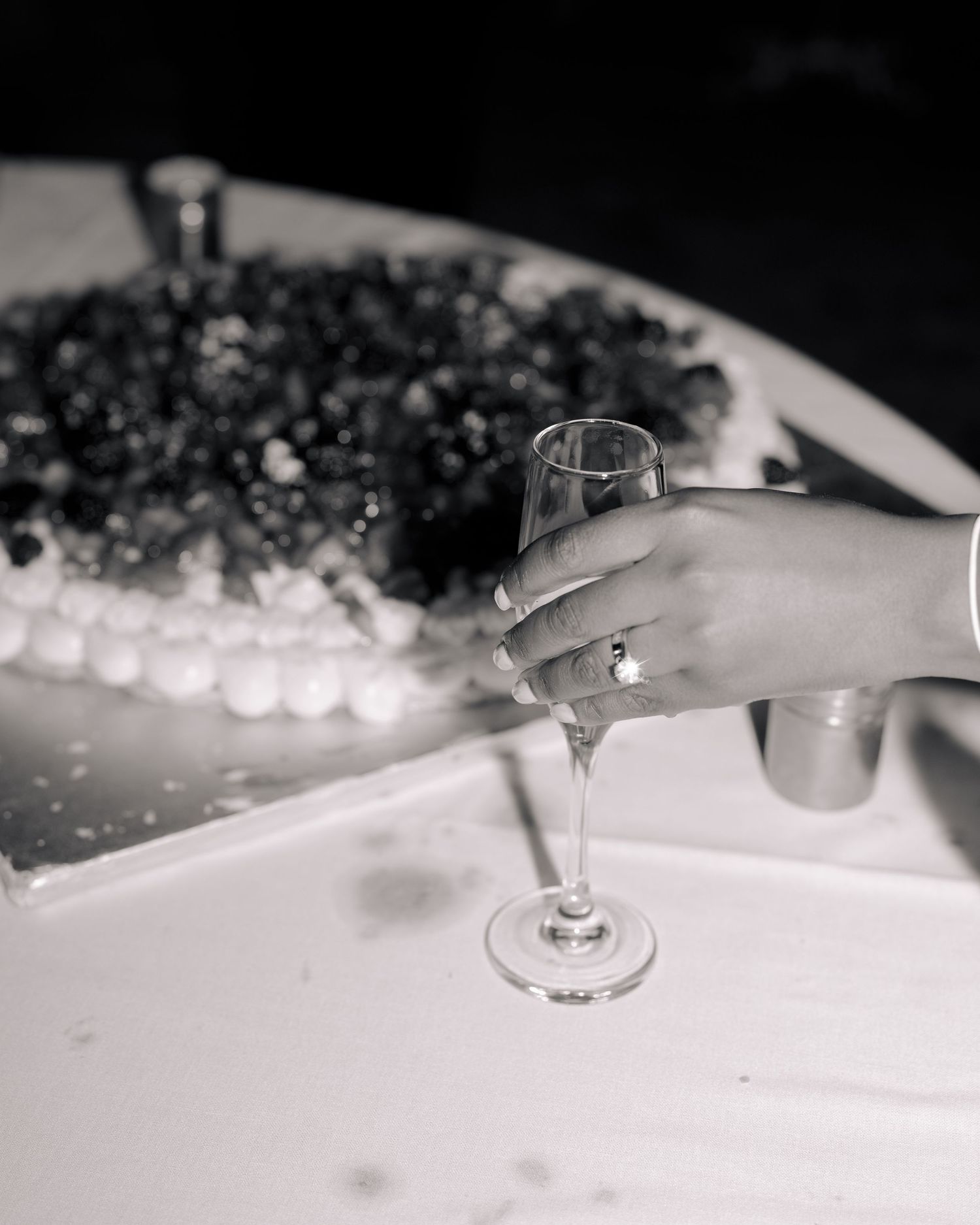 Black and white detail photo of bride holding a champagne glass with ring glistening.