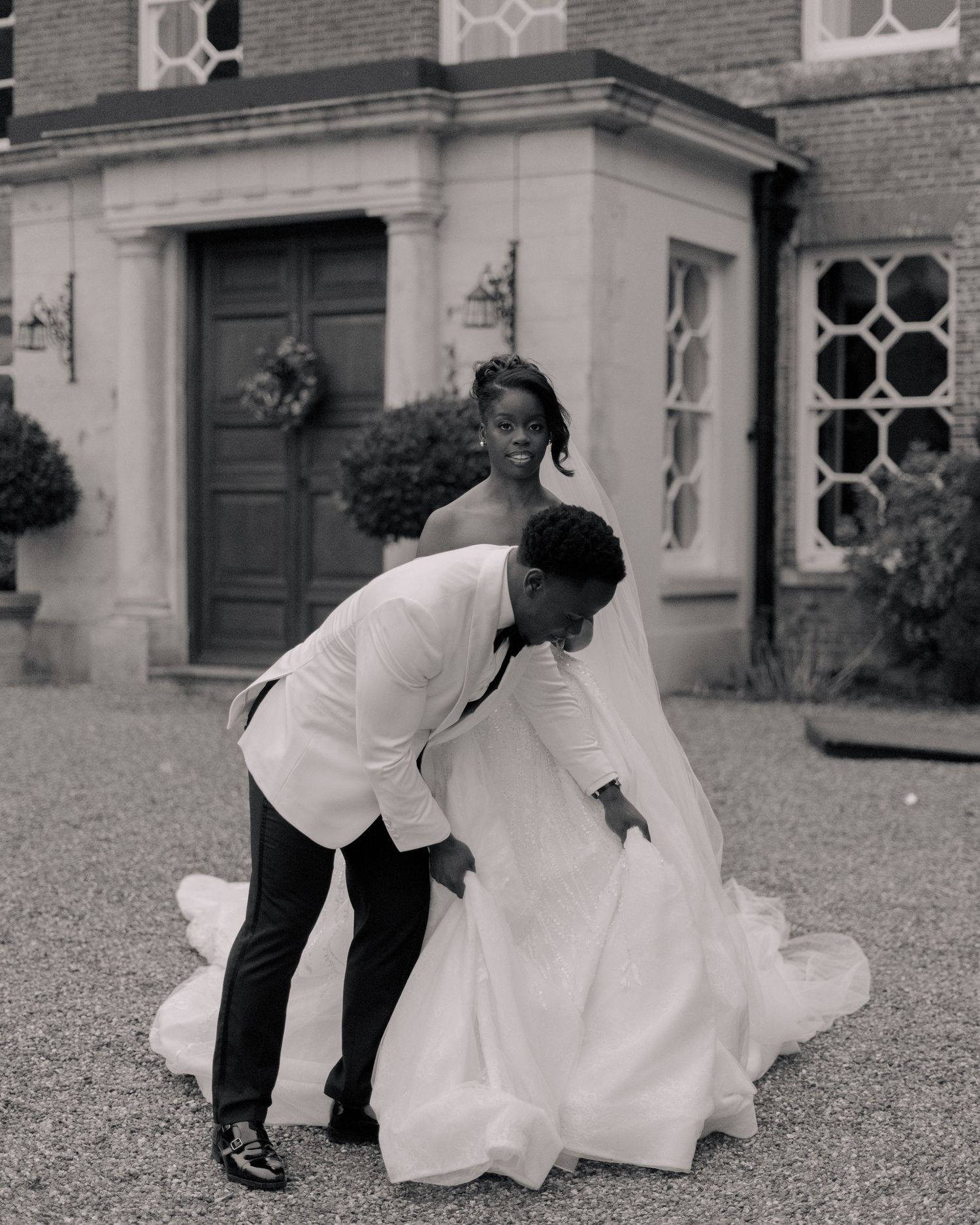 black and white picture of groom helping bride walk with long dress