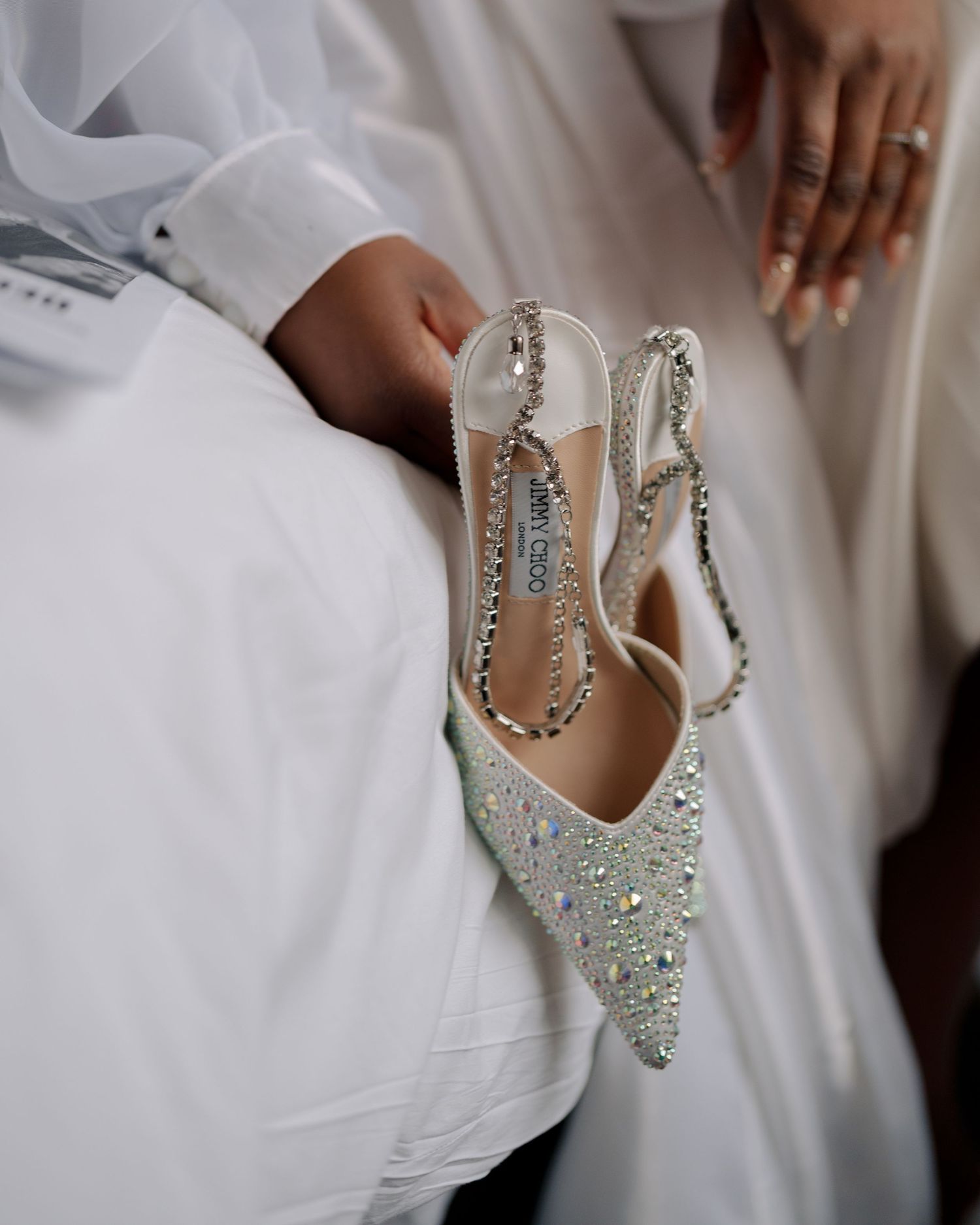 Soft and editorial close up shot of bride holding her jimmy Choo shoes by the heels as she gets ready on the morning of her wedding day