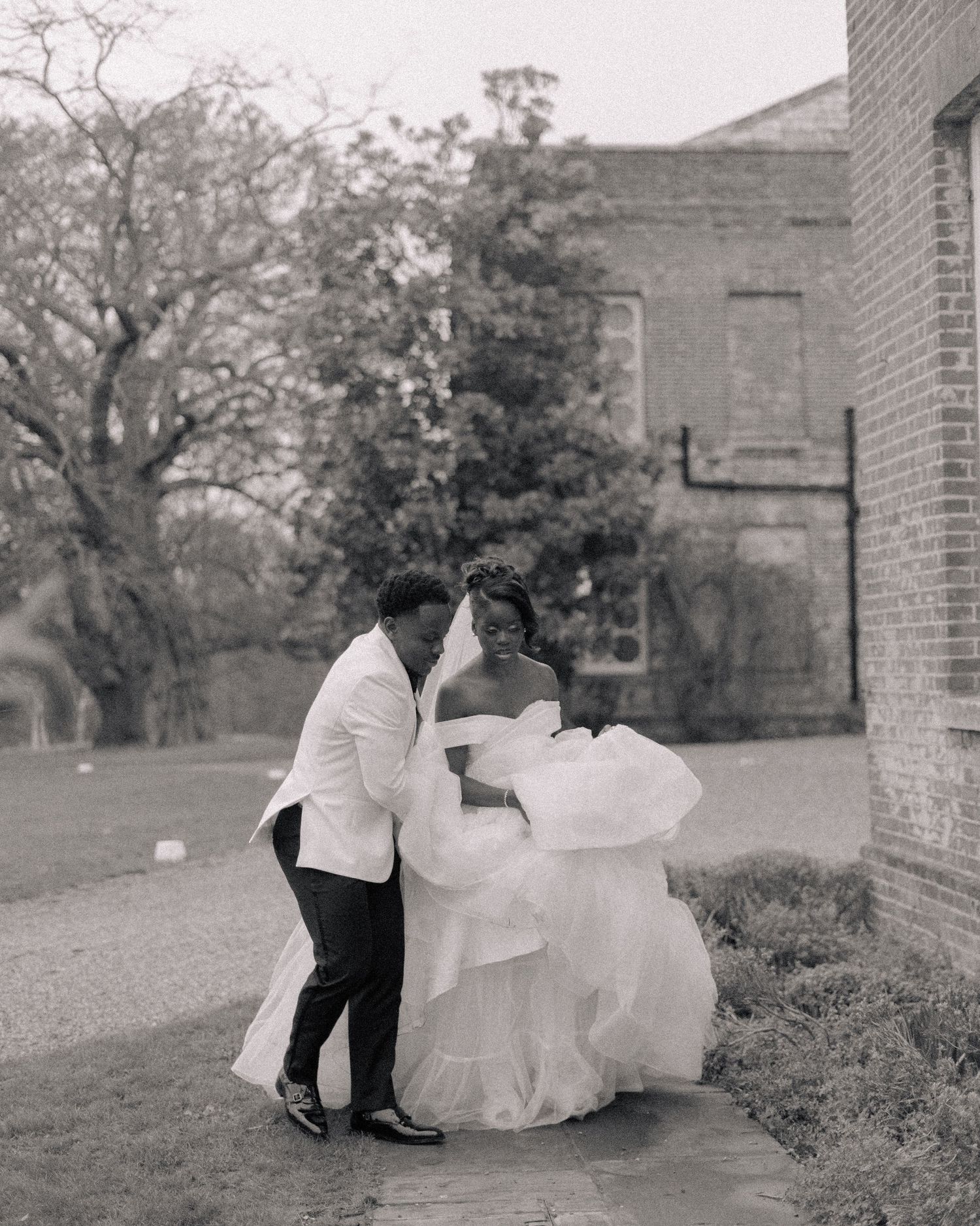 black and white picture of groom helping bride walk with long dress