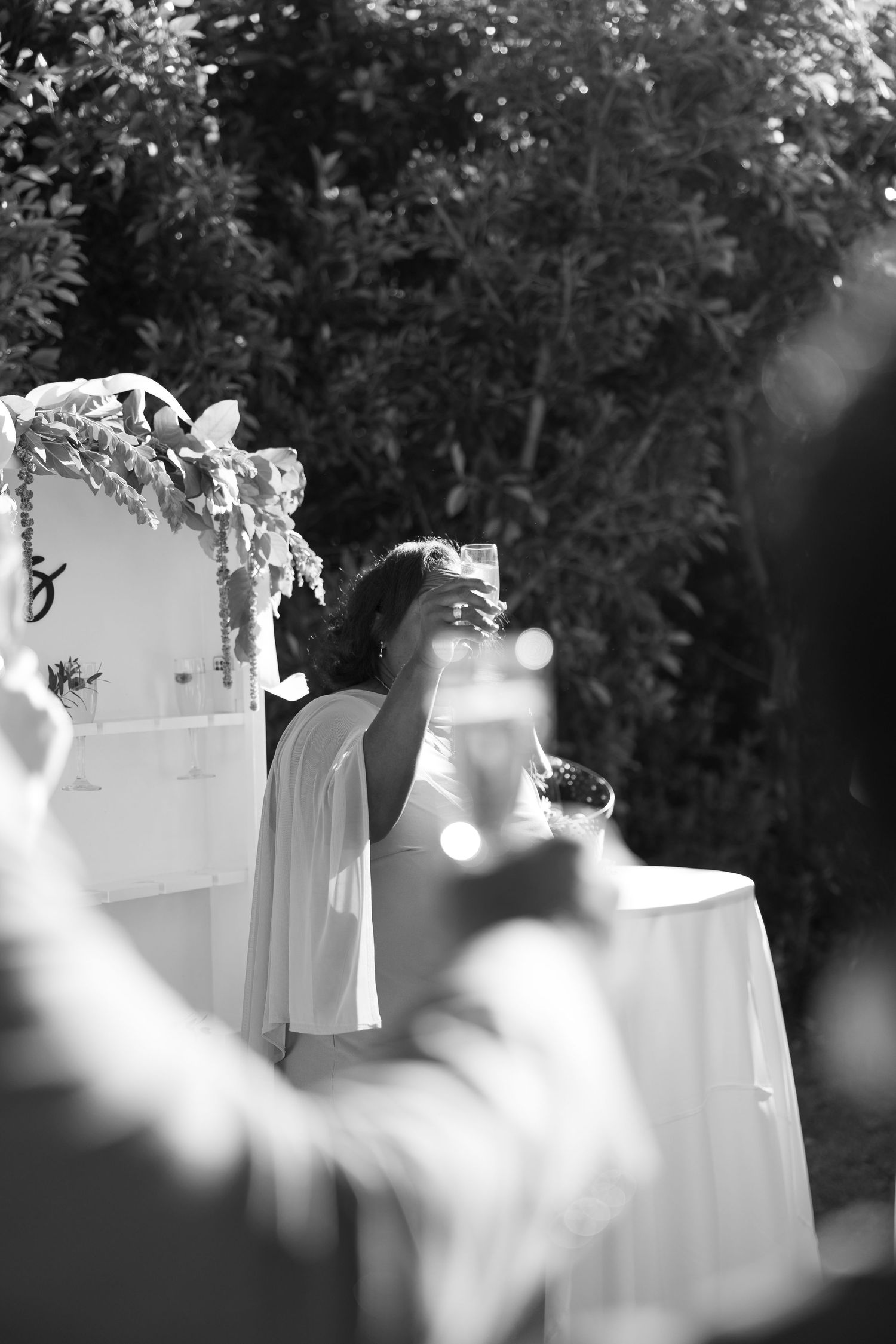 Black and white photo of a bride raising a glass in a toast at an outdoor wedding reception.