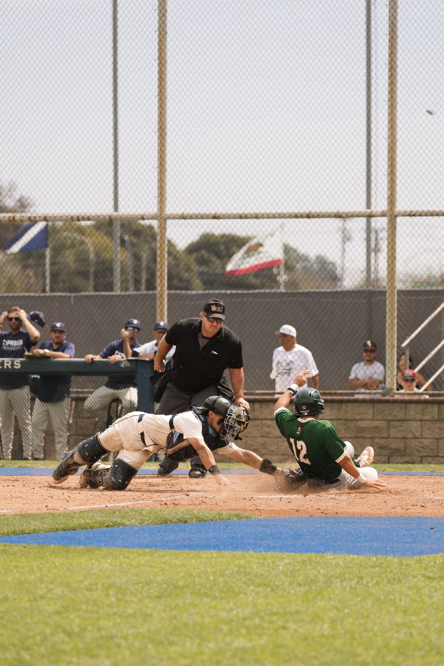 Baseball player sliding into home plate as catcher attempts tag with umpire watching closely during competitive game.