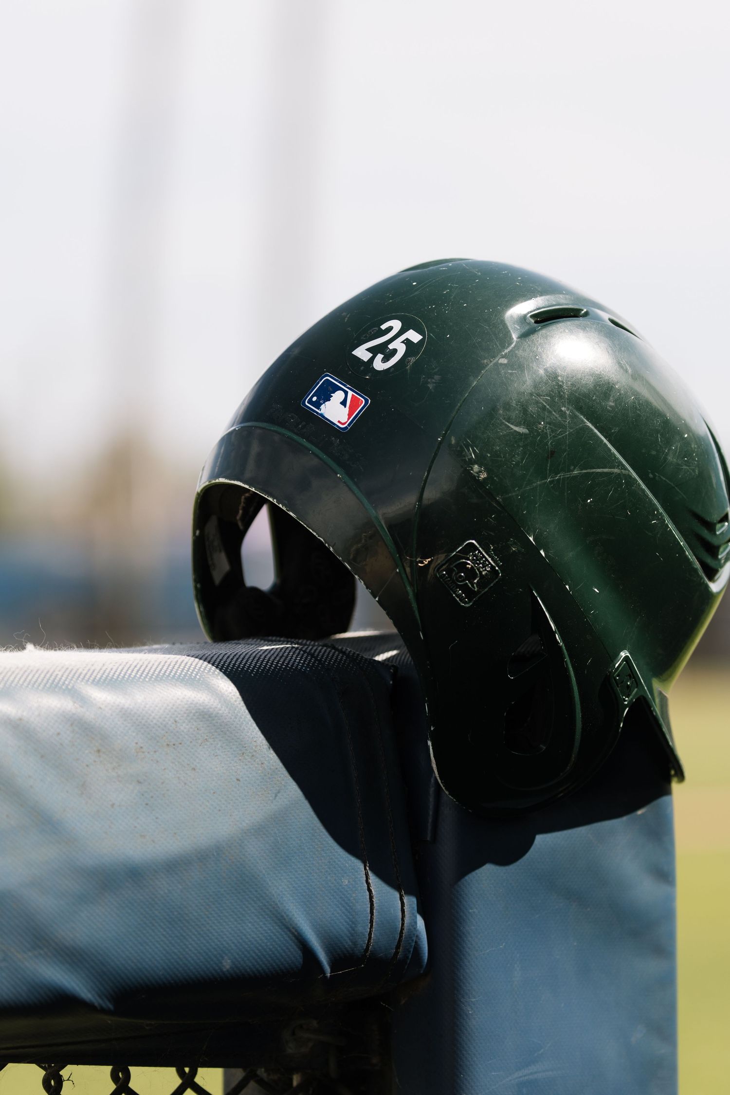 Black MLB batting helmet number 25 resting on a dugout fence at a baseball field.