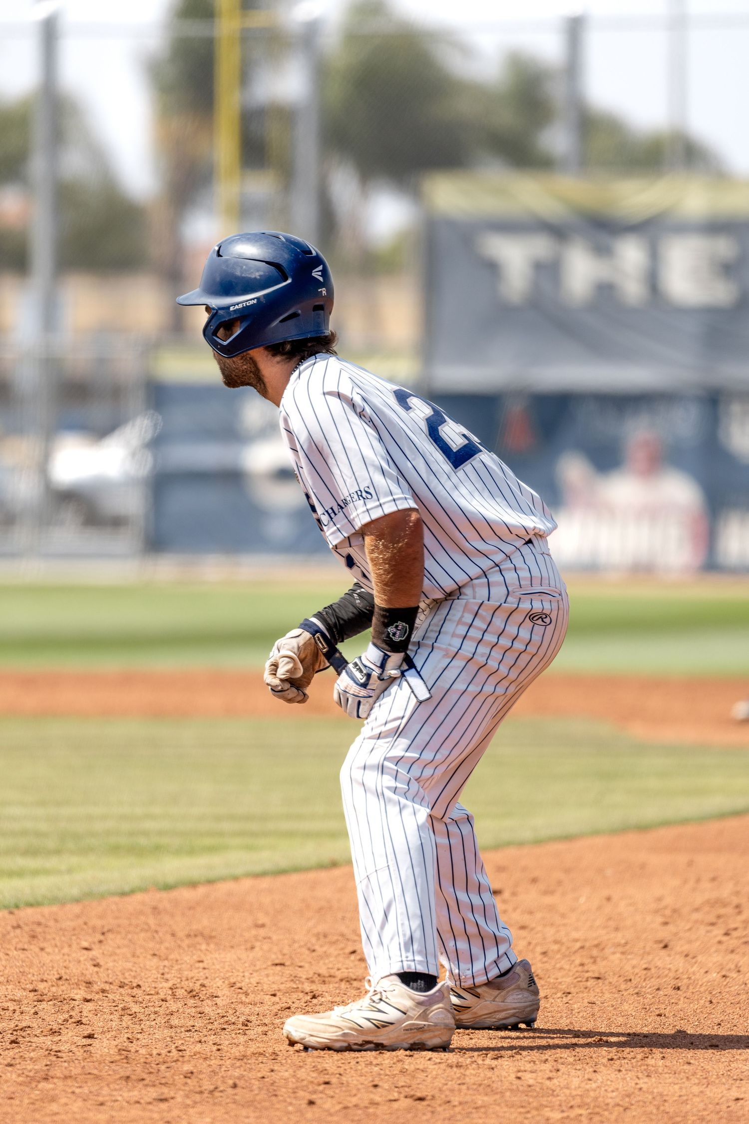 Baseball player in white pinstripe uniform takes a lead off base during a game on a sunny day.