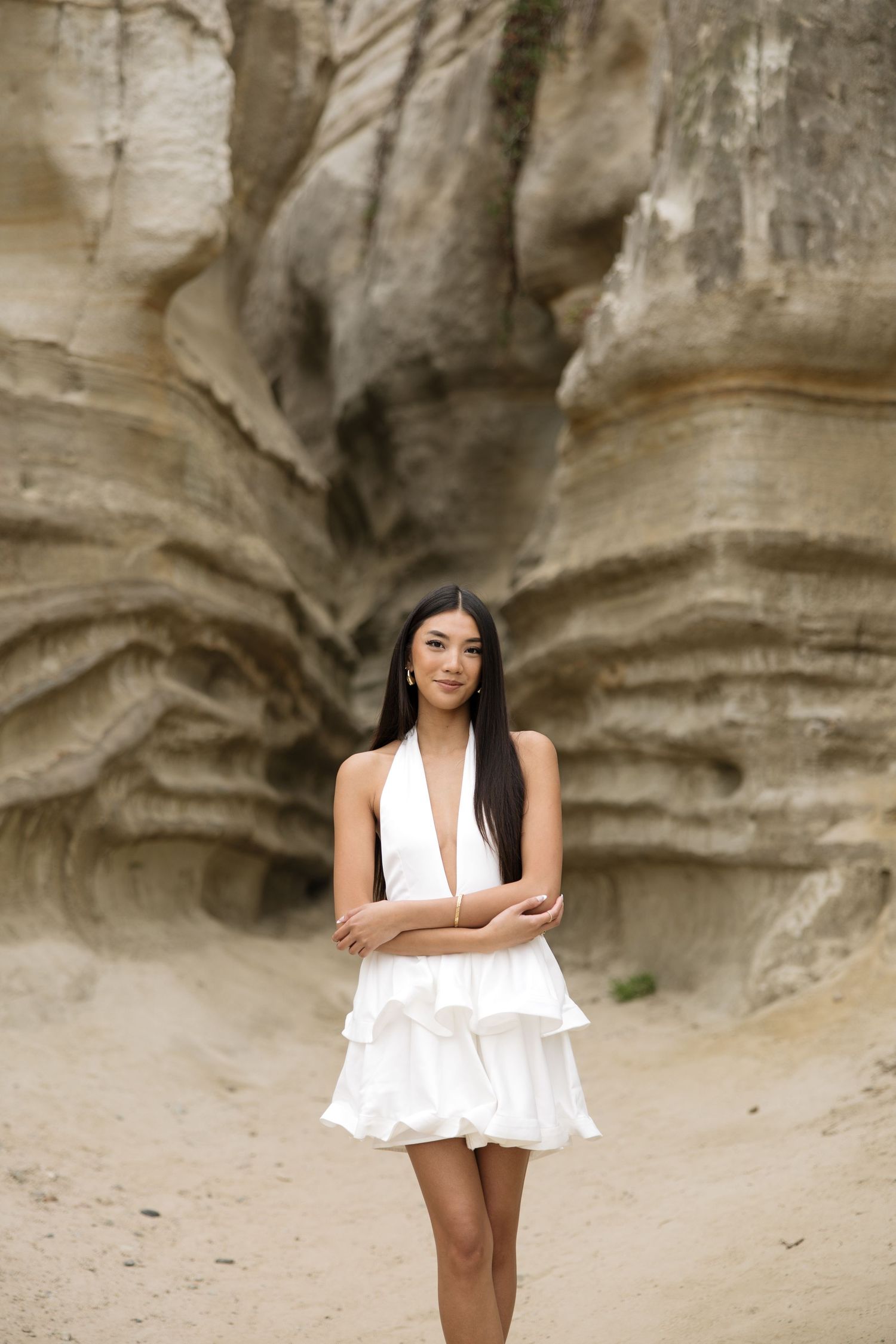 A young woman in a white halter mini dress poses gracefully in front of dramatic eroded sandstone rock formations.