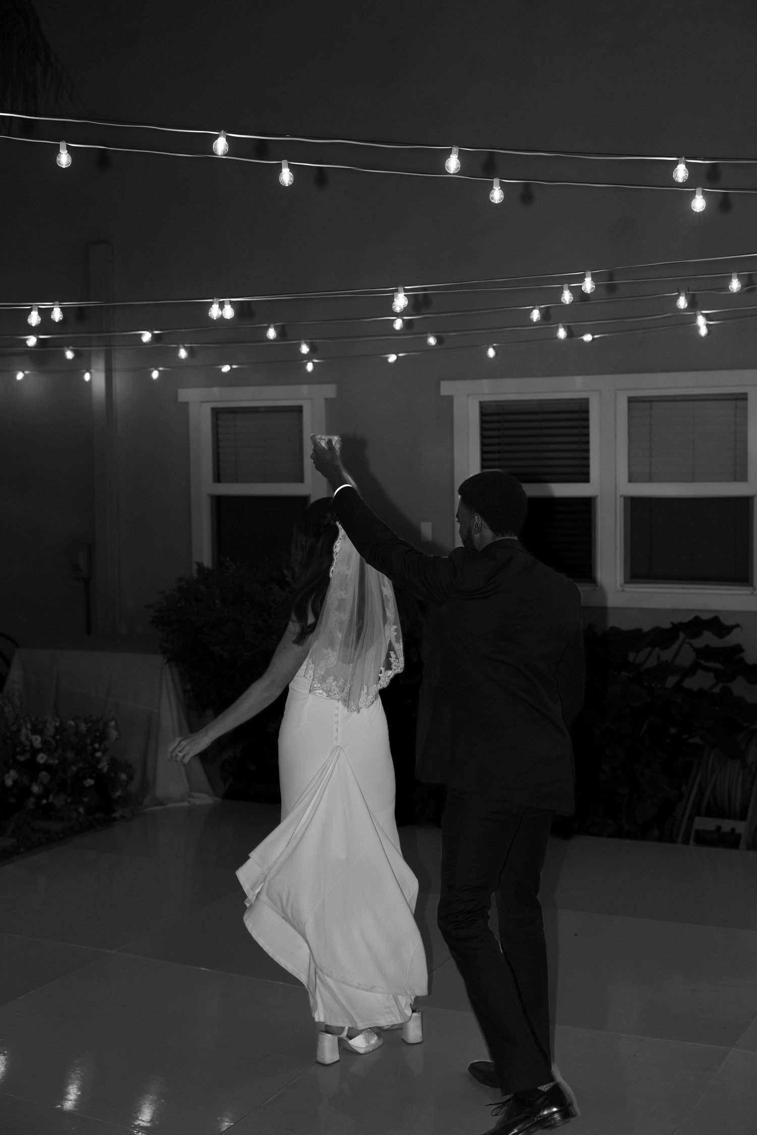 Couple dancing under string lights at nighttime wedding reception.