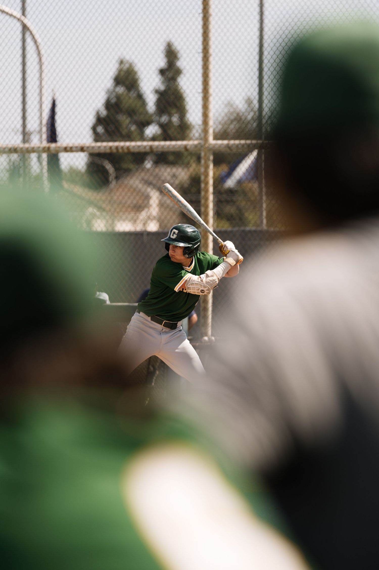Baseball batter in green uniform and helmet preparing to swing at pitch during outdoor game.